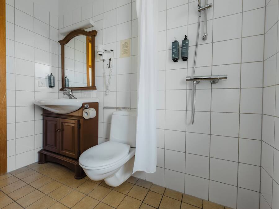 Ein Badezimmer mit weißem Waschbecken, Holzschrank, Toilette und Duschbereich mit Vorhang.