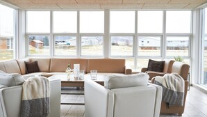 Een moderne woonkamer met een hoekbank, een salontafel en grote ramen met uitzicht op buiten.