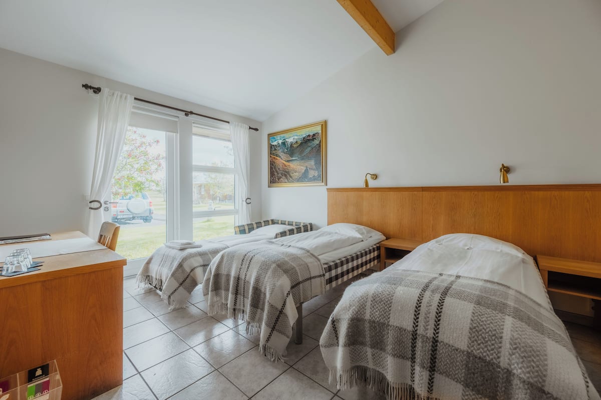 Una habitación con dos camas, un escritorio de madera y una ventana con cortinas.