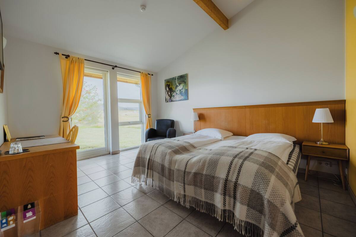 Un dormitorio con cama, escritorio, silla, mesita de noche y ventana con cortinas.