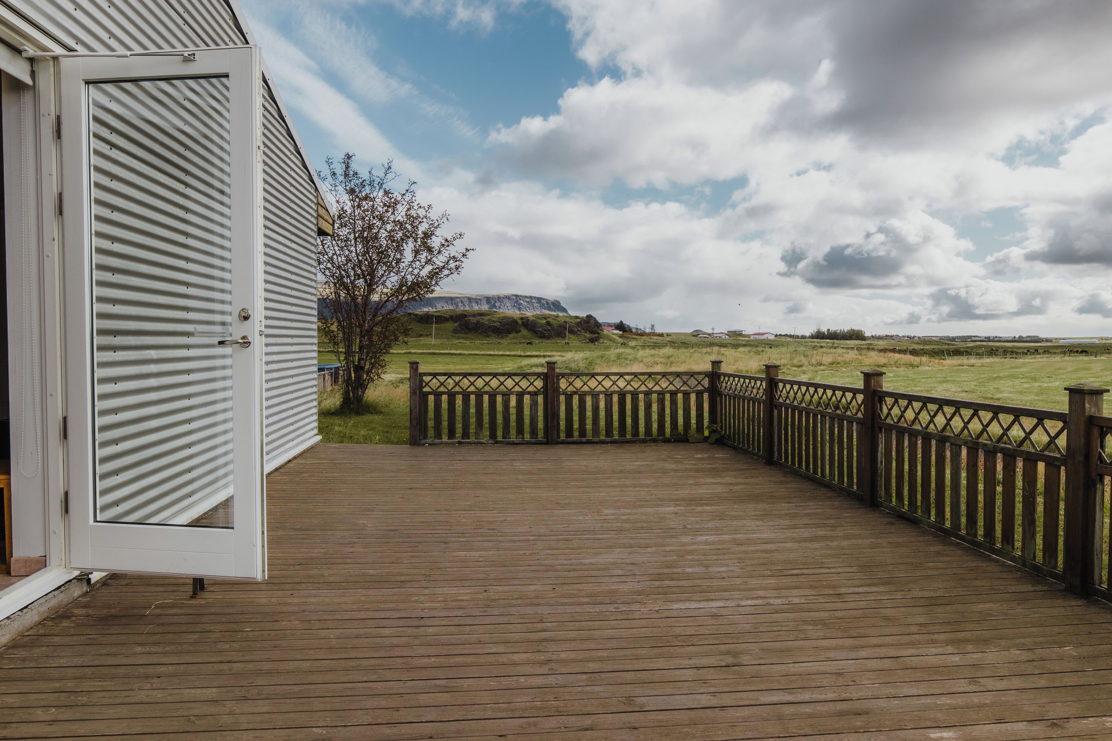 A wooden deck with a view of a grassy field and distant hills.