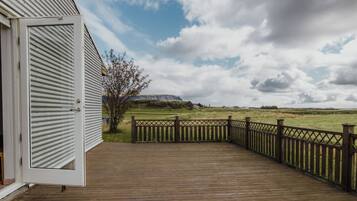 A wooden deck with a view of a grassy field and distant hills.