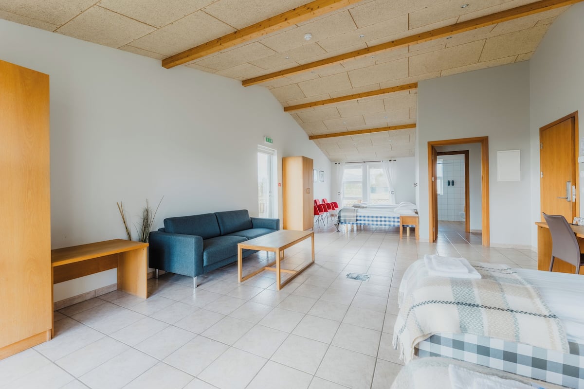 Una habitación de hotel espaciosa con una cama grande, un sofá, un banco de madera y un comedor con sillas rojas.