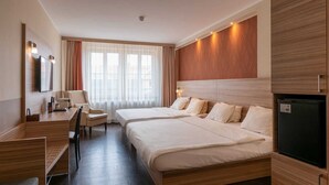 A hotel room with two beds, a desk, a chair, a TV, and a refrigerator.