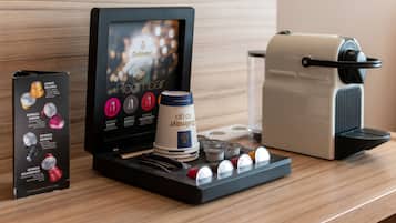 Une machine à café, comprenant un écran, un compartiment pour les capsules de café et une cafetière, est posée sur une surface en bois.
