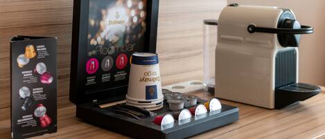 A coffee machine setup with a display screen, a coffee pod holder, and a coffee maker on a wooden surface.