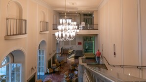A spacious lobby with a grand chandelier, multiple seating areas, and a staircase leading to an upper level.