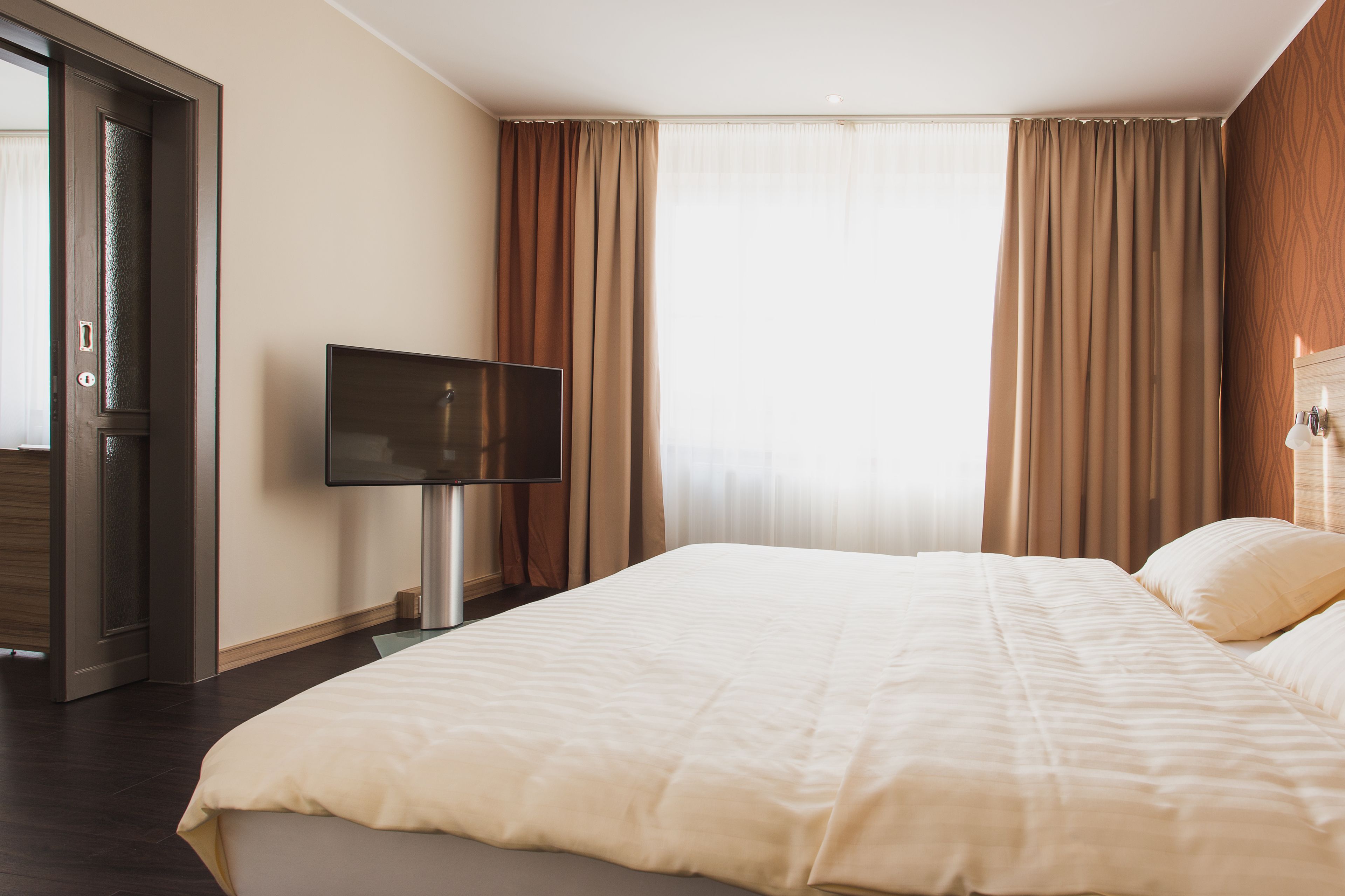 Ein Hotelzimmer mit einem großen Bett, einem Flachbildfernseher und einer Holztür.