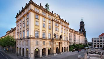Ein historisches Gebäude mit klassischer Architektur, mit mehreren Bögen und einem markanten Glockenturm im Hintergrund.