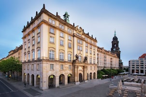 A historic building with classical architecture, featuring multiple arches and a prominent clock tower in the background.