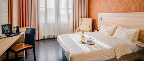 Habitación de hotel con una cama de madera, un escritorio con una computadora, una silla y una ventana con cortinas.