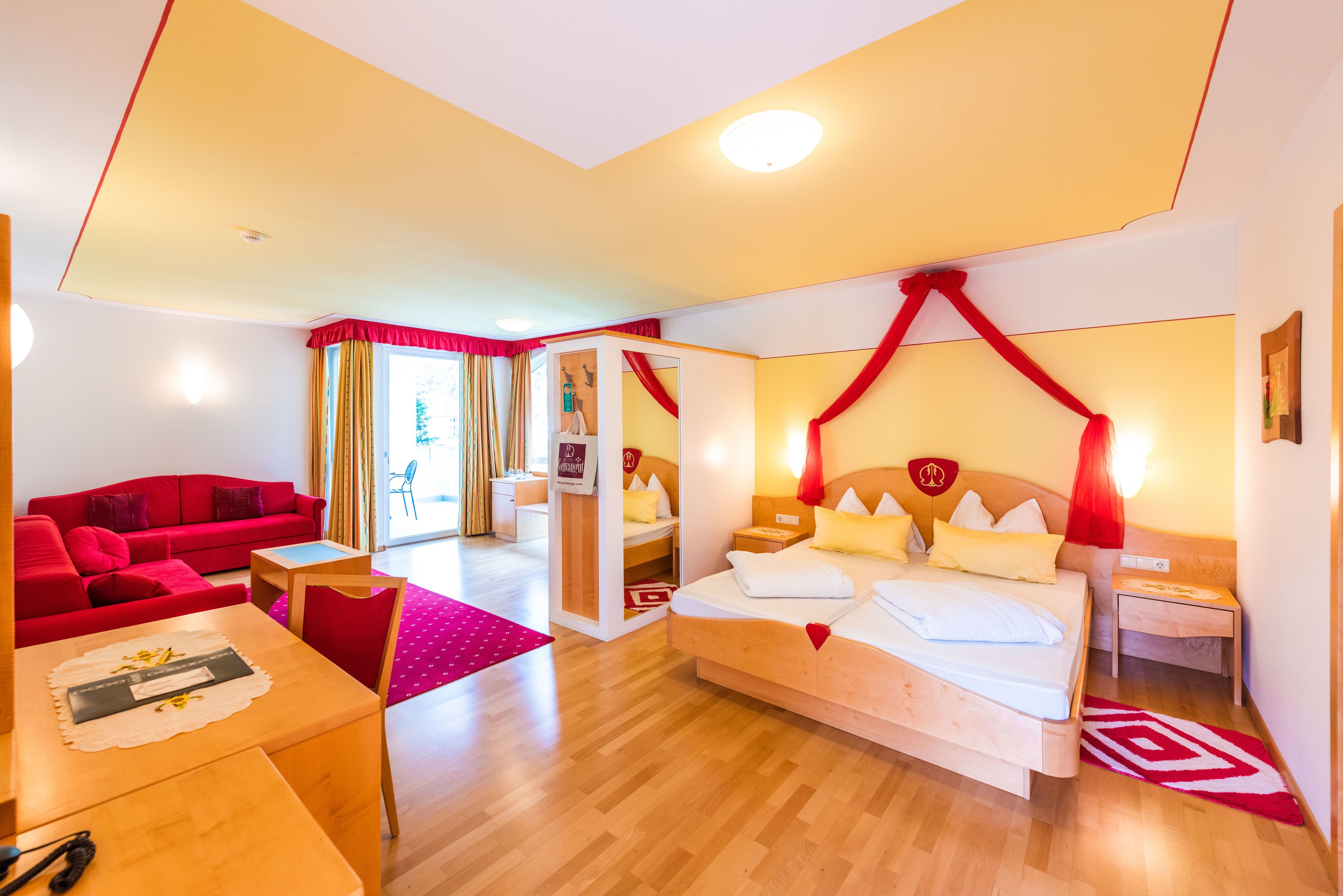 A hotel room with a bed, a red sofa, a wooden table, and a desk.
