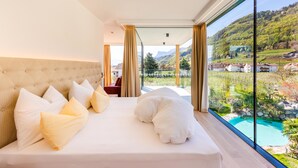 A bedroom with a large bed, a view of a swimming pool, and a scenic outdoor landscape. - Hotel Gschwangut (Lana)