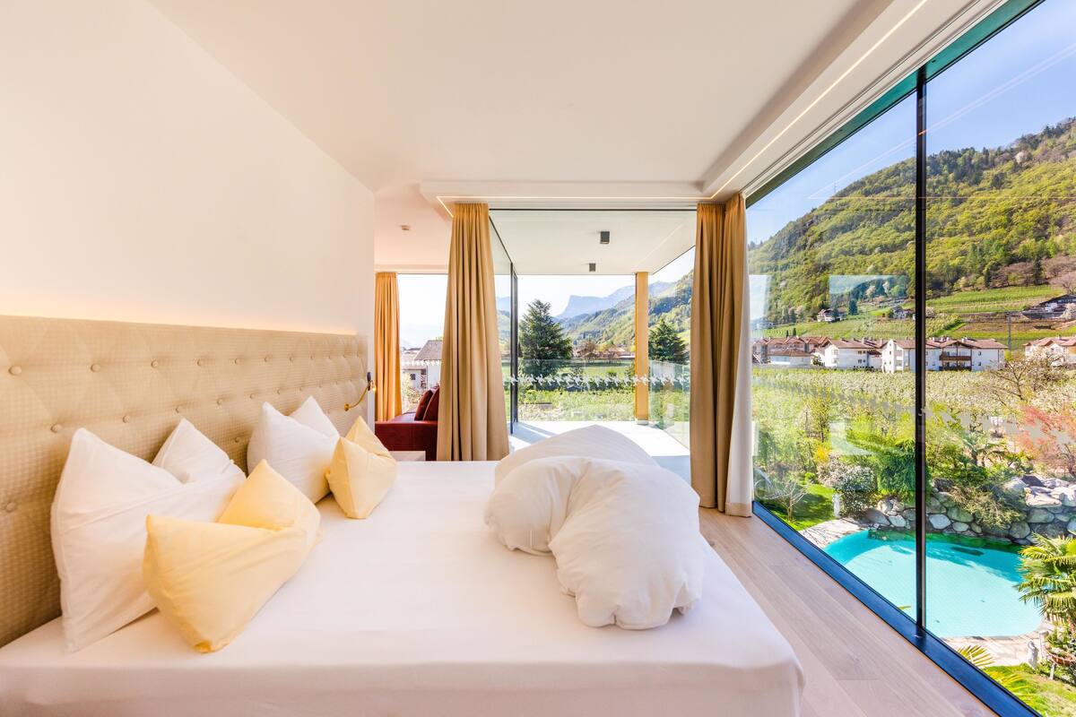 A bedroom with a large bed, a view of a swimming pool, and a scenic outdoor landscape.