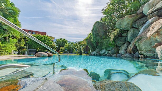 A clear swimming pool with a metal ladder, surrounded by large rocks and greenery. - Hotel Gschwangut (Lana)