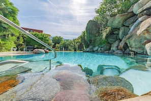 A clear swimming pool with a metal ladder, surrounded by large rocks and greenery. - Hotel Gschwangut (Lana)
