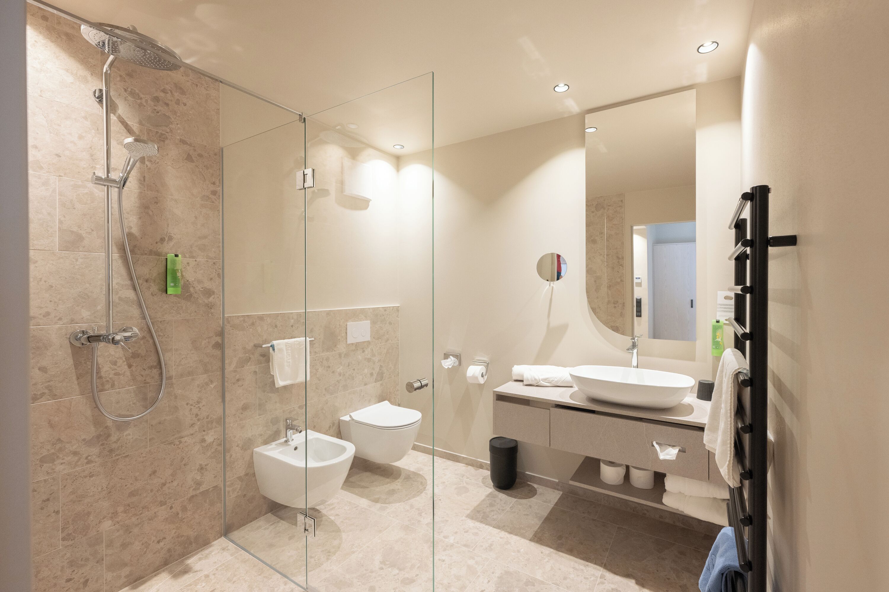 Een moderne badkamer met een douchecabine van glas, een bidet, toilet, wastafel en spiegel.