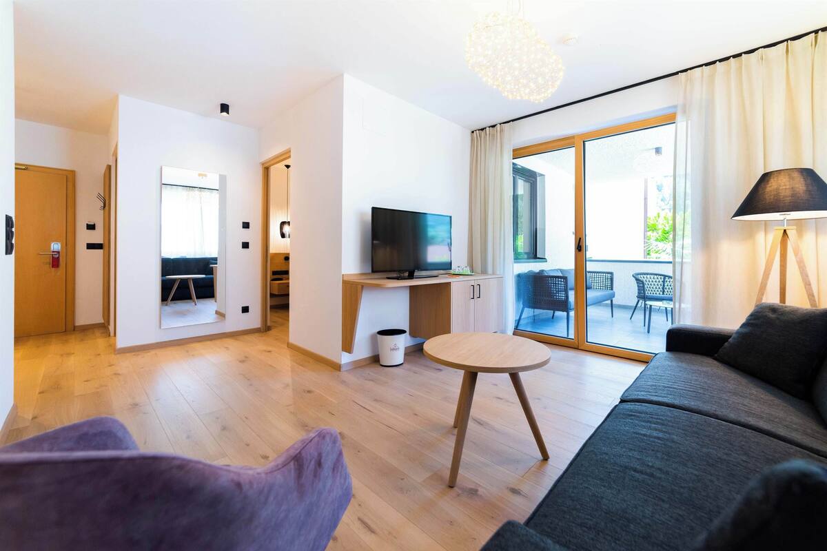 A modern living room with a sofa, a small round table, a TV, and a sliding glass door leading to an outdoor area.