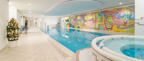An indoor swimming pool with a colorful mural, a hot tub, and a Christmas tree.