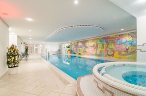 An indoor swimming pool with a colorful mural, a hot tub, and a Christmas tree. - Hotel Gschwangut (Lana)
