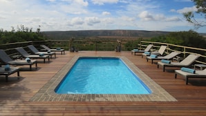 Una piscina rectangular con cubierta de madera y sillones de descanso.
