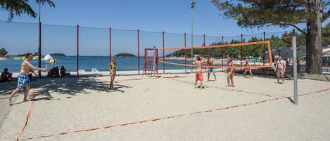 A beach volleyball court with a net, surrounded by sand and trees.
