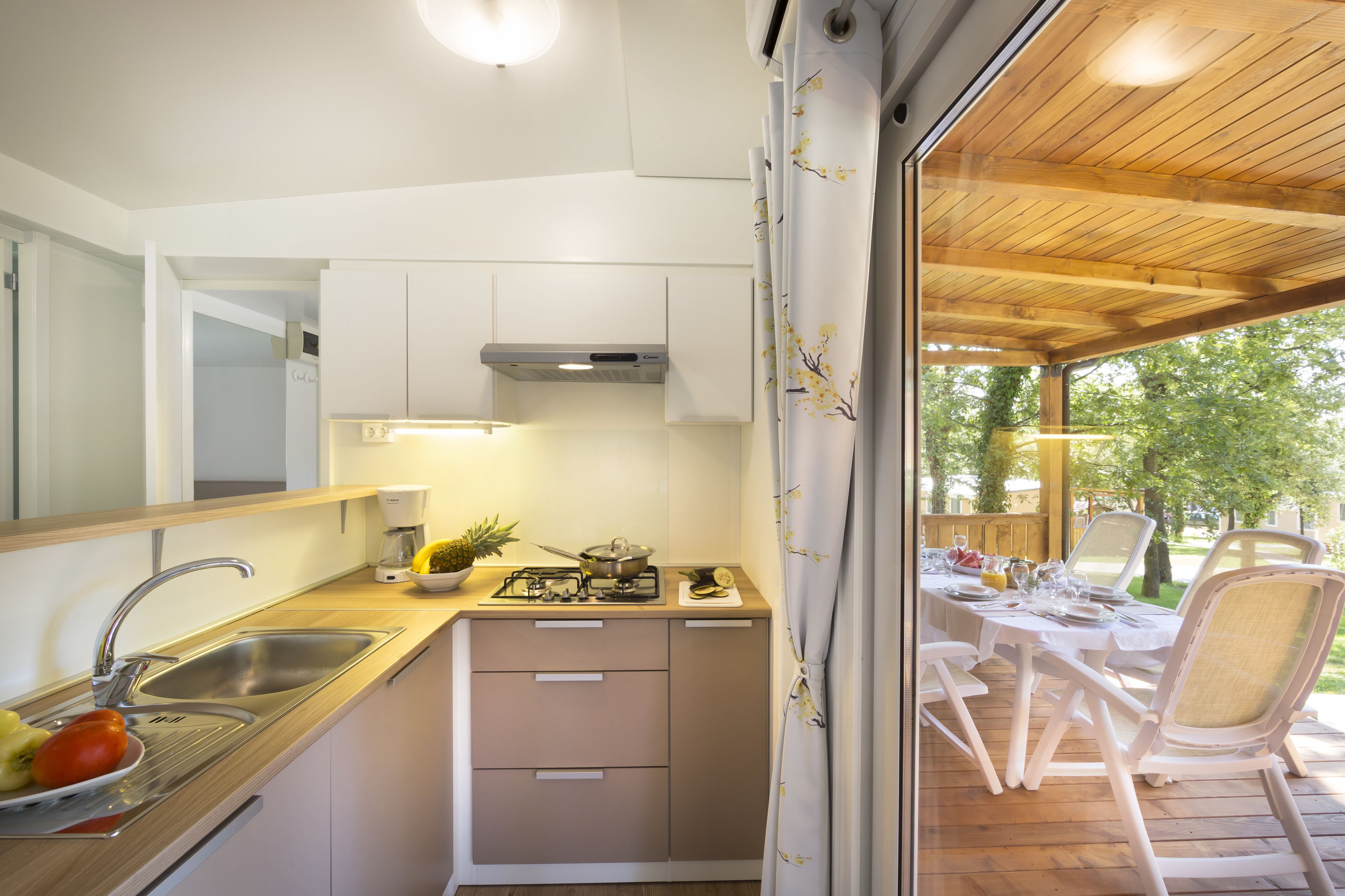 A compact kitchen with a sink, stove, and cabinets, leading to an outdoor dining area with a table and chairs.