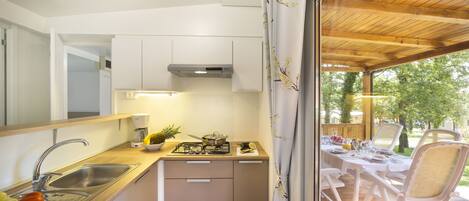A compact kitchen with a sink, stove, and cabinets, leading to an outdoor dining area with a table and chairs.