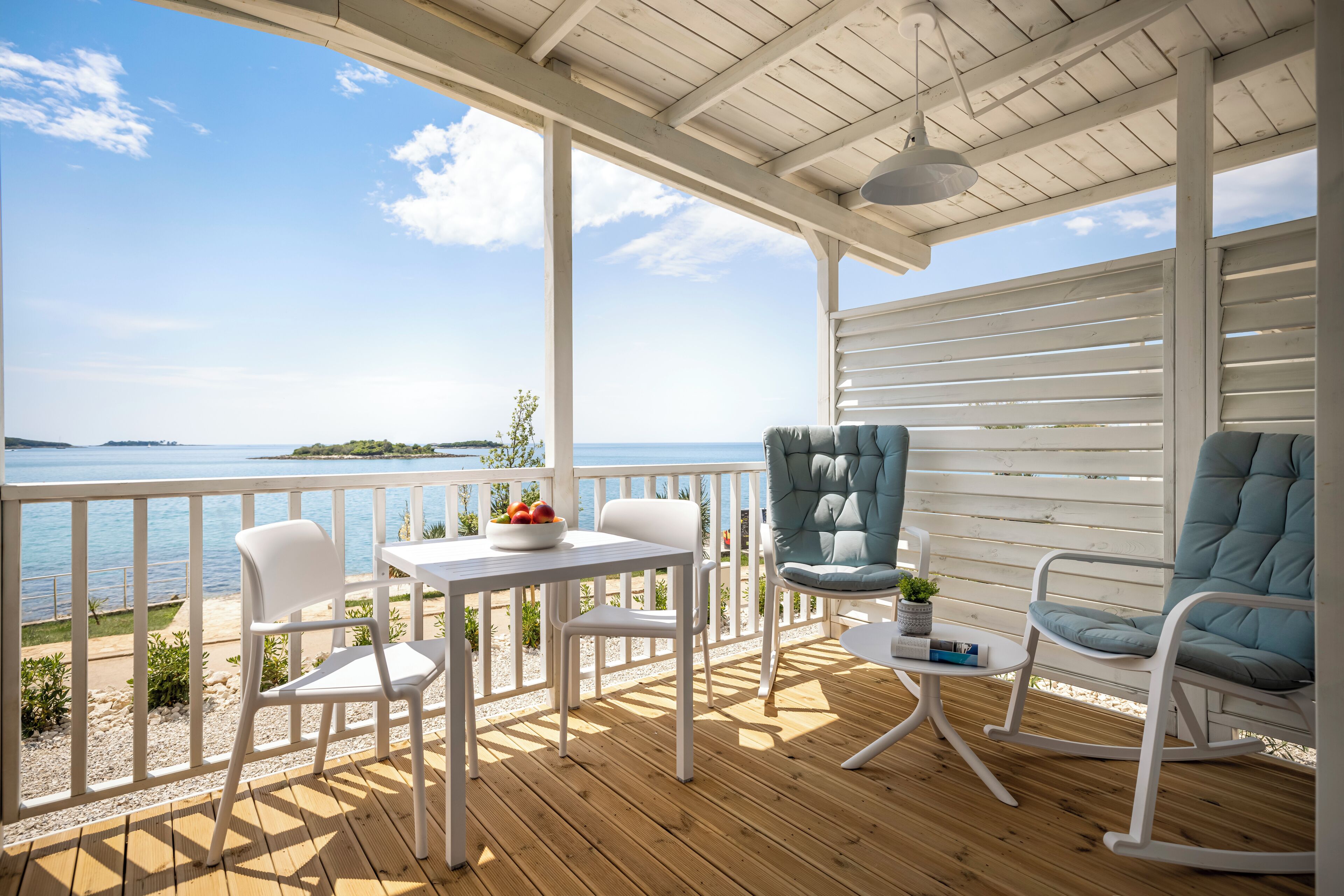 Une terrasse en bois avec une balustrade blanche, une table avec des chaises et une vue sur la mer.