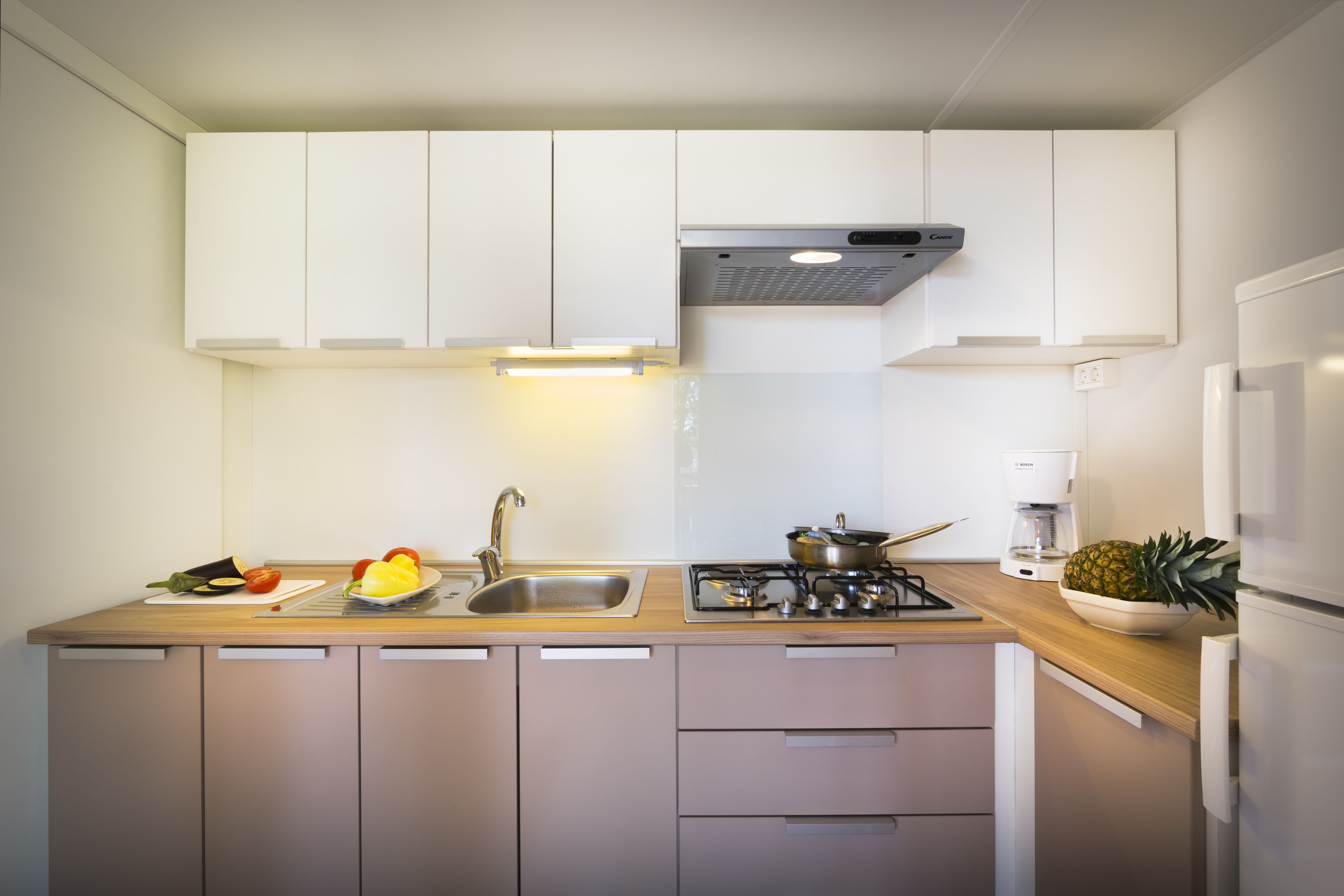 A modern kitchen with white cabinets, a stainless steel sink, a gas stove, and a coffee maker.
