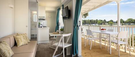 Ein modernes Wohnzimmer mit einer Couch, einem Essbereich mit Tisch und Stühlen, einem an der Wand montierten Fernseher und Blick ins Freie.
