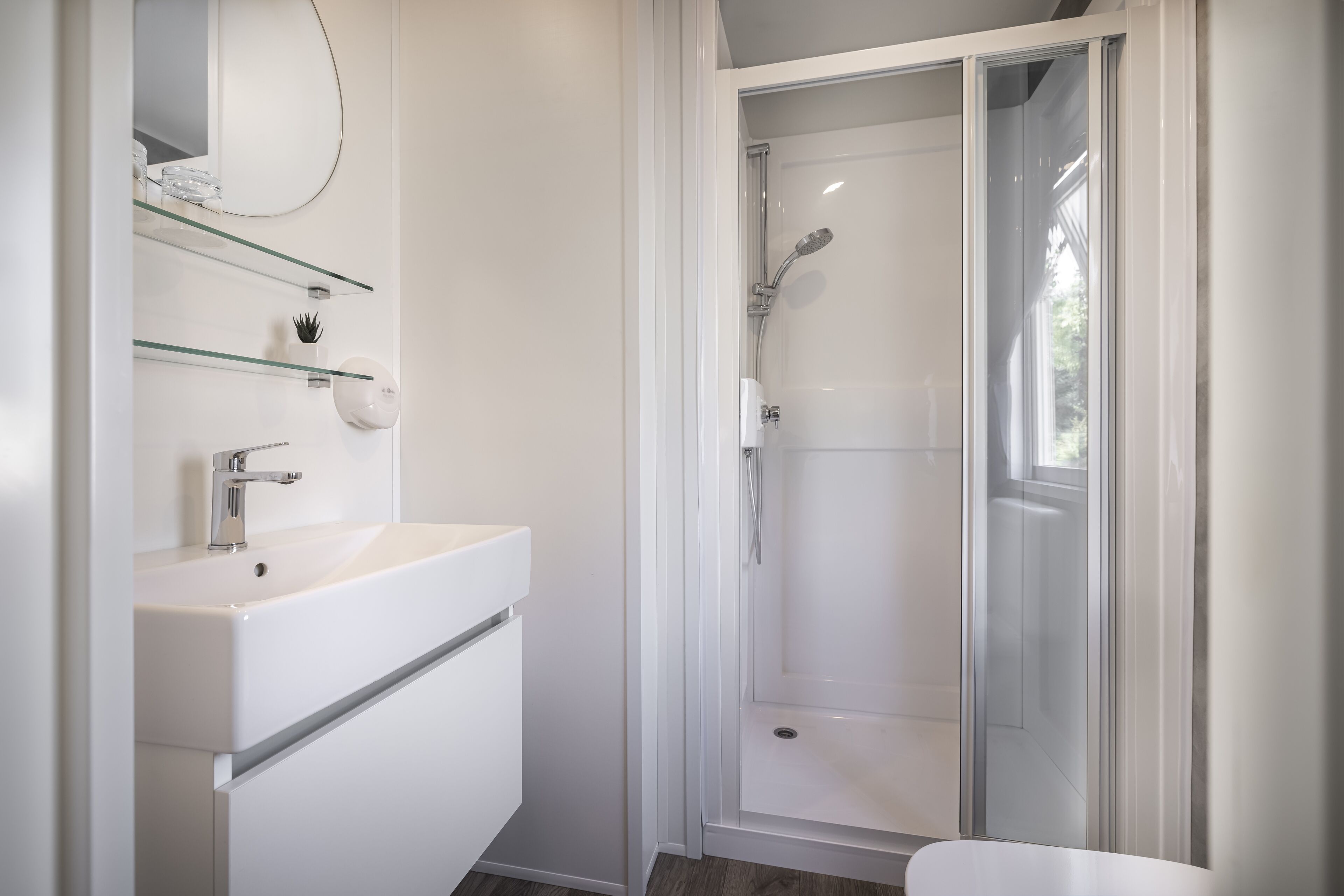 Une salle de bain moderne avec un lavabo blanc, des étagères en verre et une douche à parois de verre.