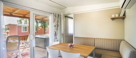 A modern room with a wooden table, white chairs, a cushioned bench, and a sliding glass door leading to an outdoor area with a patio and a view of a neighboring house.