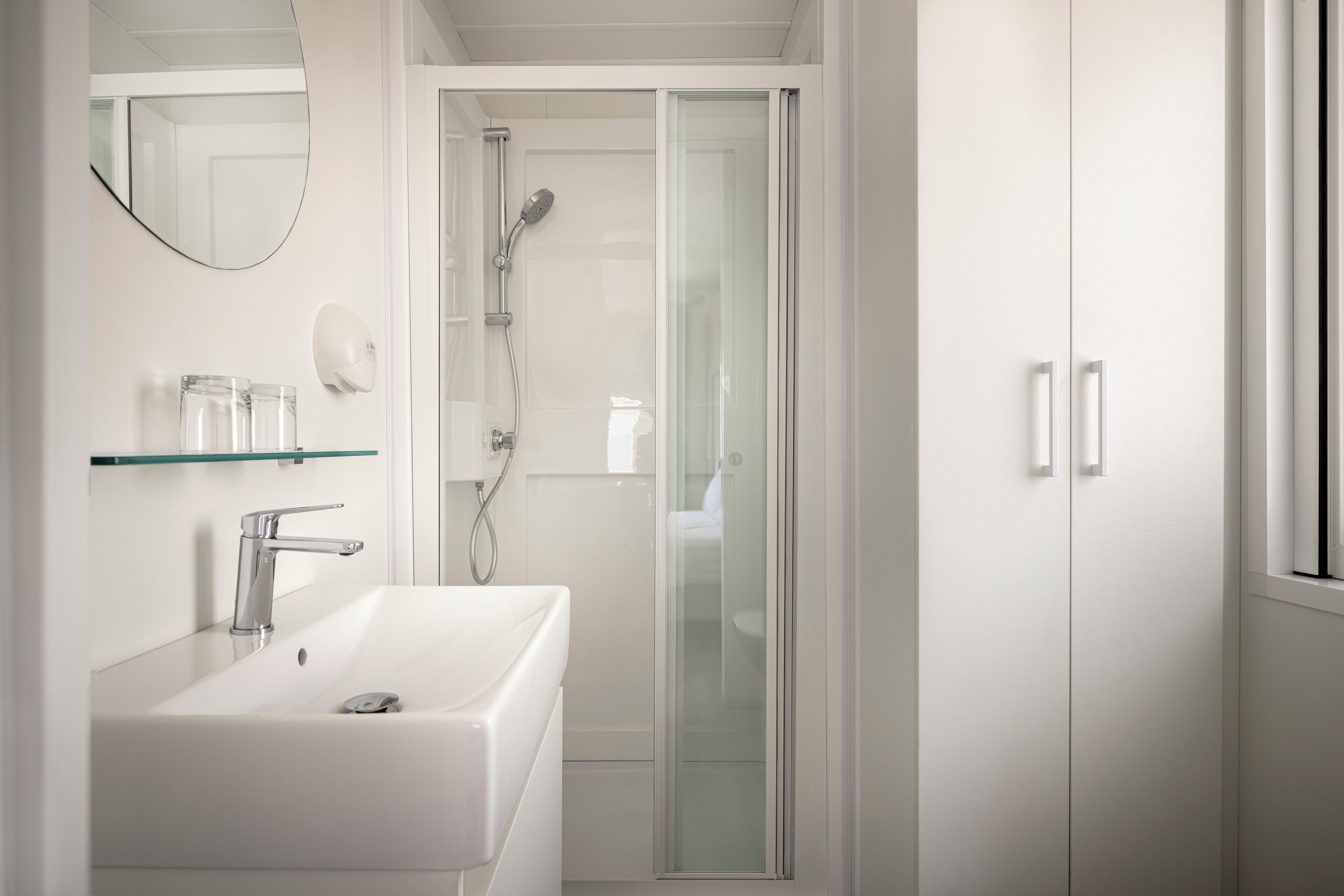 A modern bathroom with a white sink, glass shower enclosure, and a mirror above the sink.