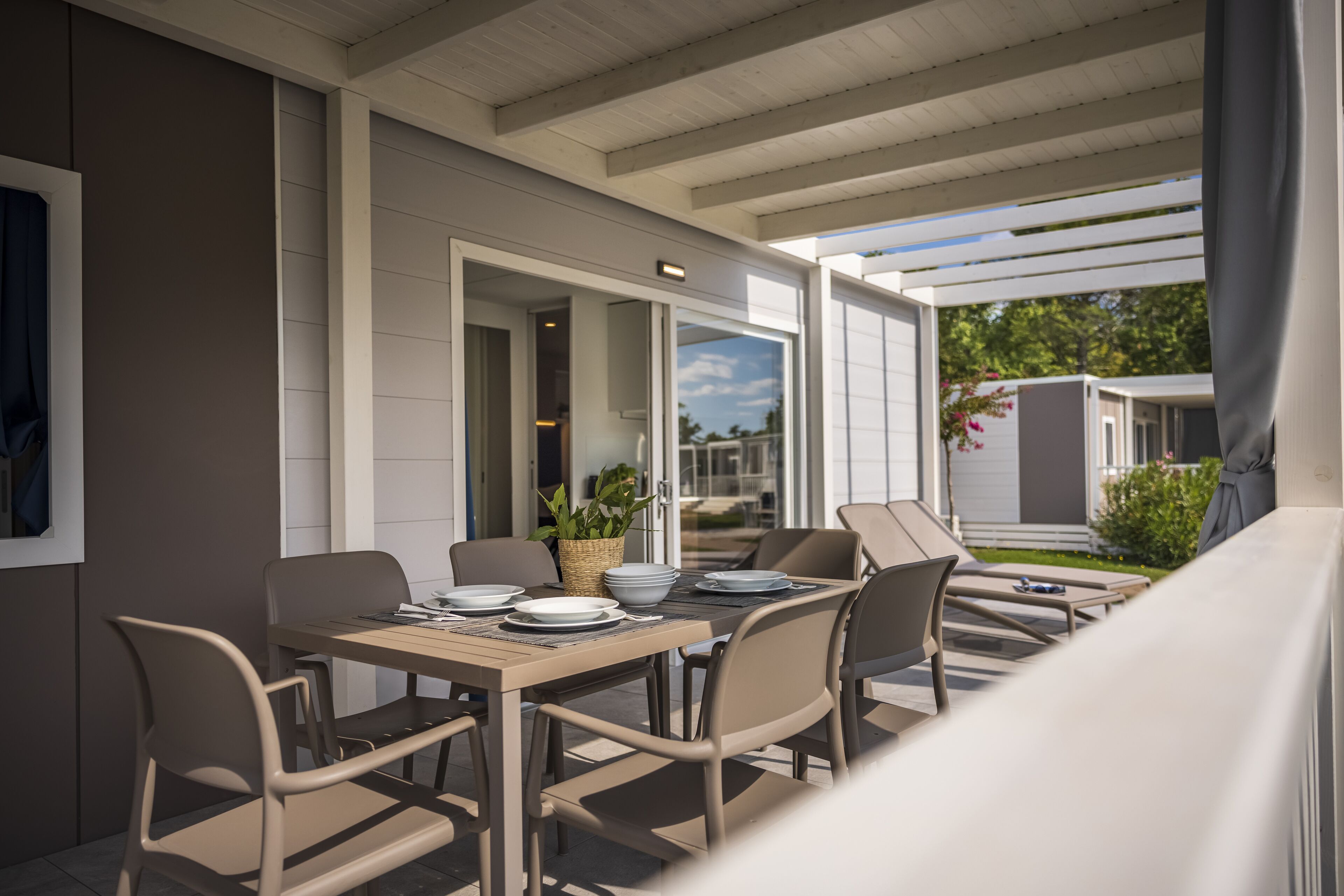 An outdoor patio with a table set for dining, surrounded by chairs, and a covered area with a view of neighboring houses.