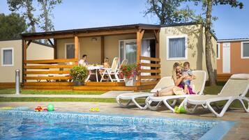Ein Poolbereich mit Liegestühlen, einem Esstisch und einer überdachten Terrasse.