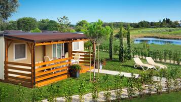 A wooden cabin with a deck, two lounge chairs, and a view of a lake.