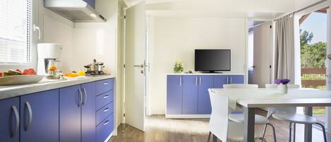 A modern kitchen with blue cabinets, a white dining table, and a TV in the background.