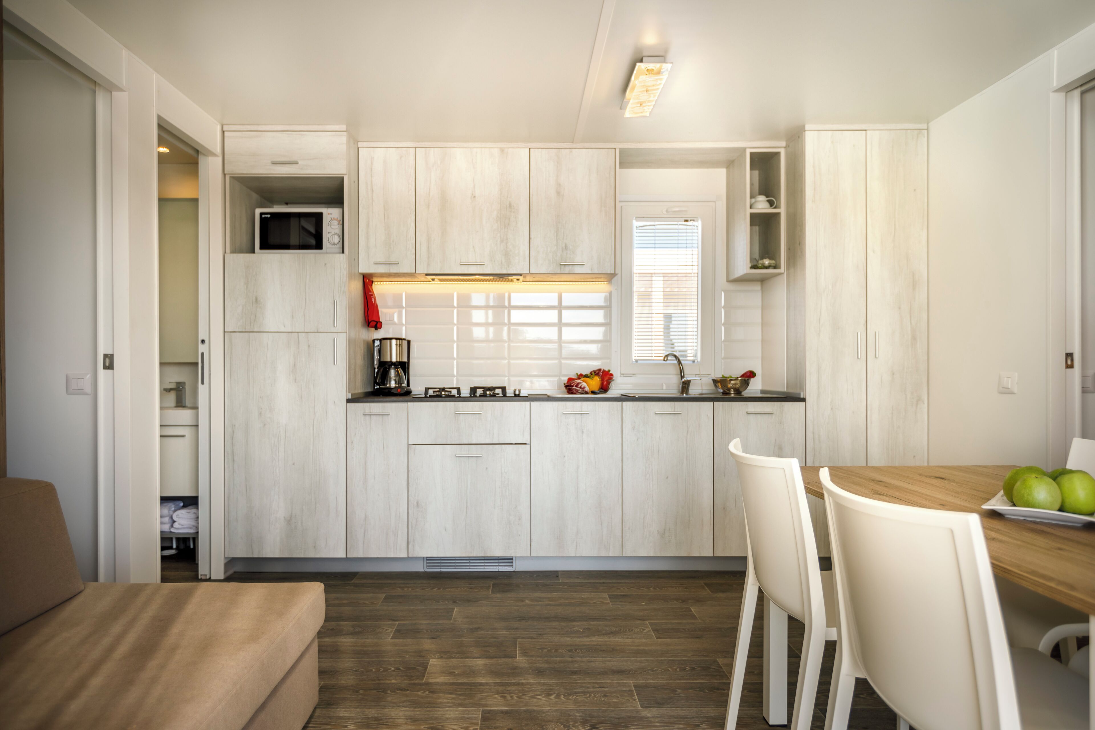 A compact kitchen with white cabinetry, a microwave, and a dining area with a wooden table and white chairs.