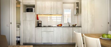 A compact kitchen with white cabinetry, a microwave, and a dining area with a wooden table and white chairs.