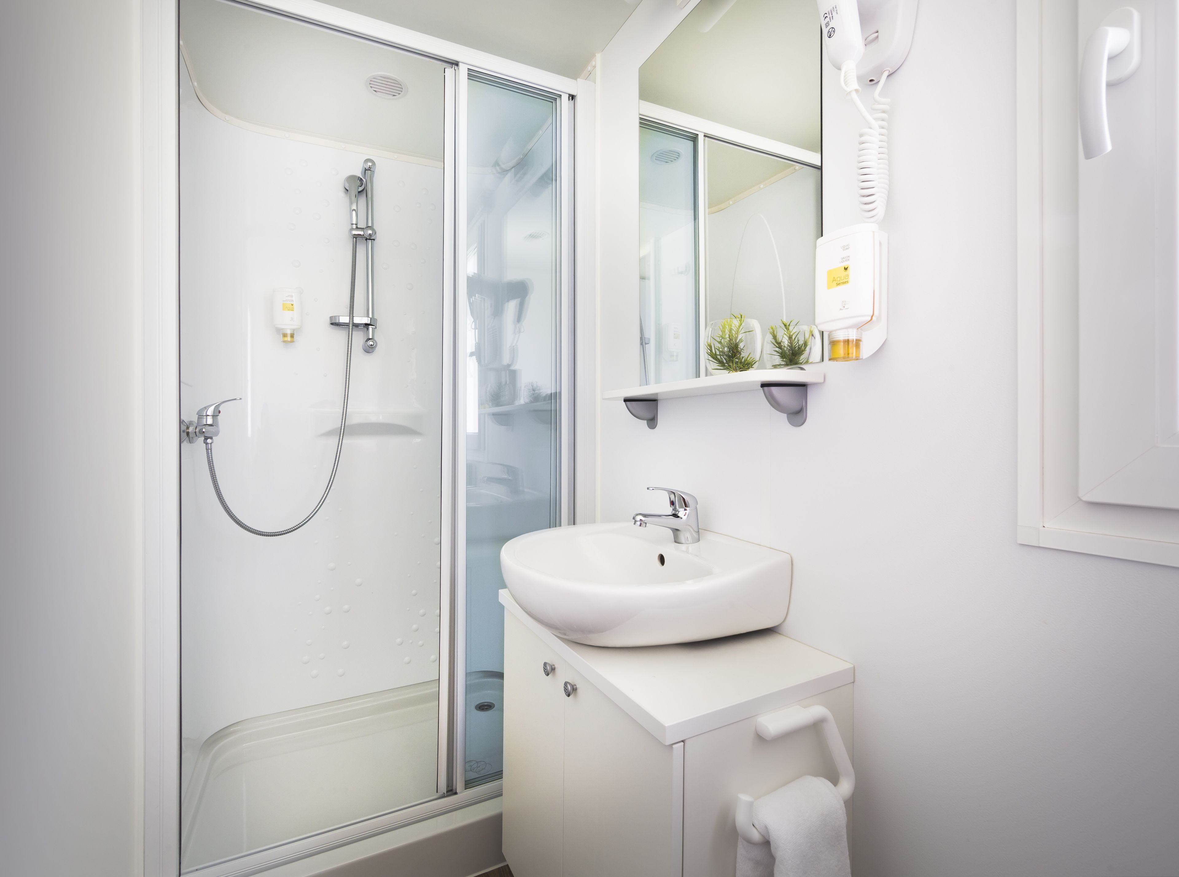 A modern bathroom with a glass shower enclosure, a white sink, and a mirror with a mounted hairdryer.