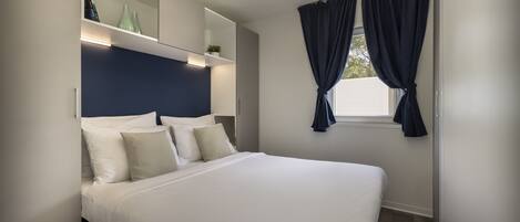 A modern bedroom with a large bed, a built-in nightstand, a mirror, and a window with curtains.