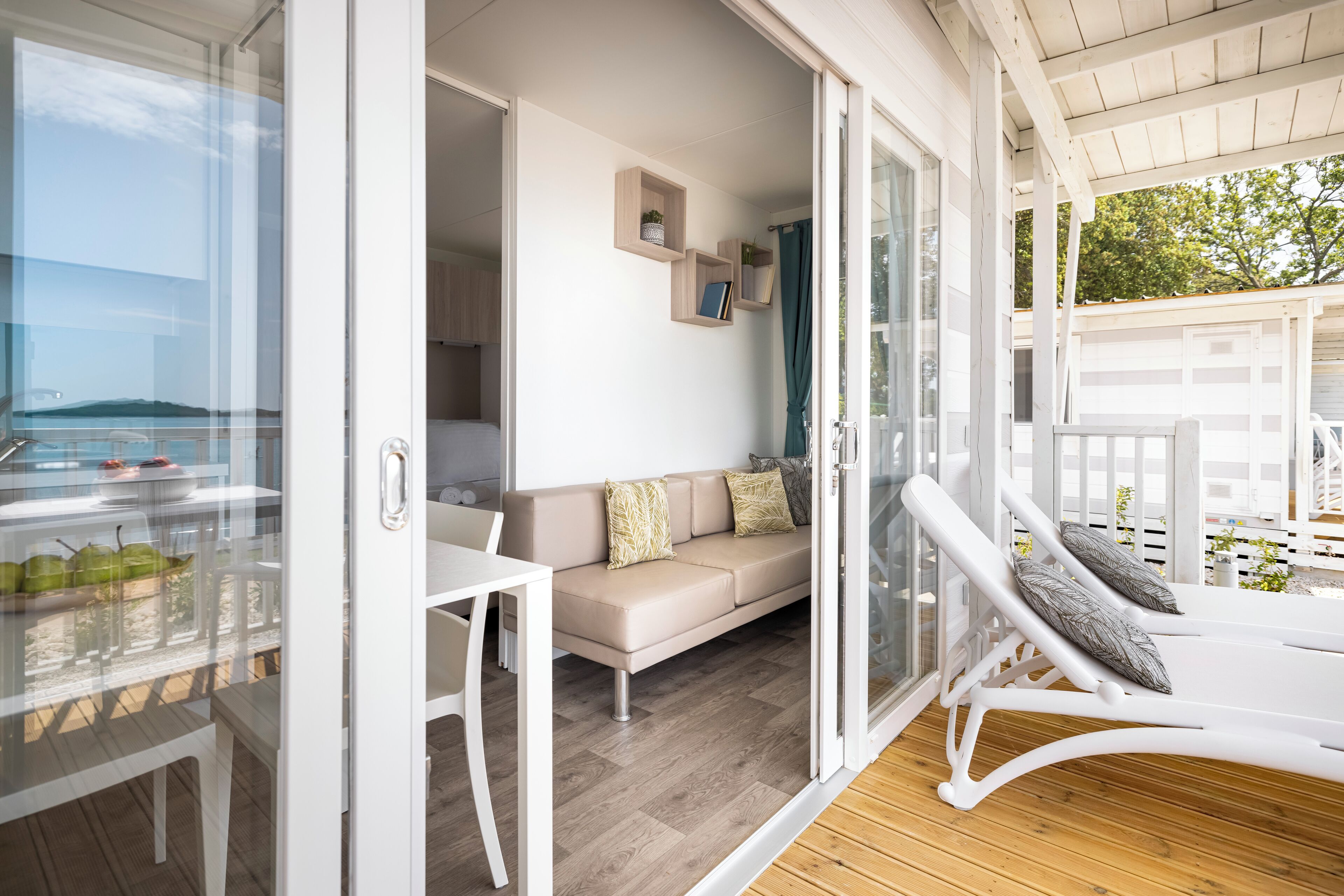 A modern living area with a glass door leading to a balcony, a sofa, a lounge chair, and a small table.