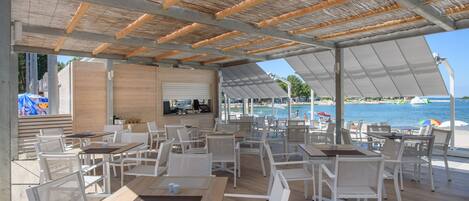 An outdoor dining area with white chairs and tables, a wooden deck, and a view of the sea.