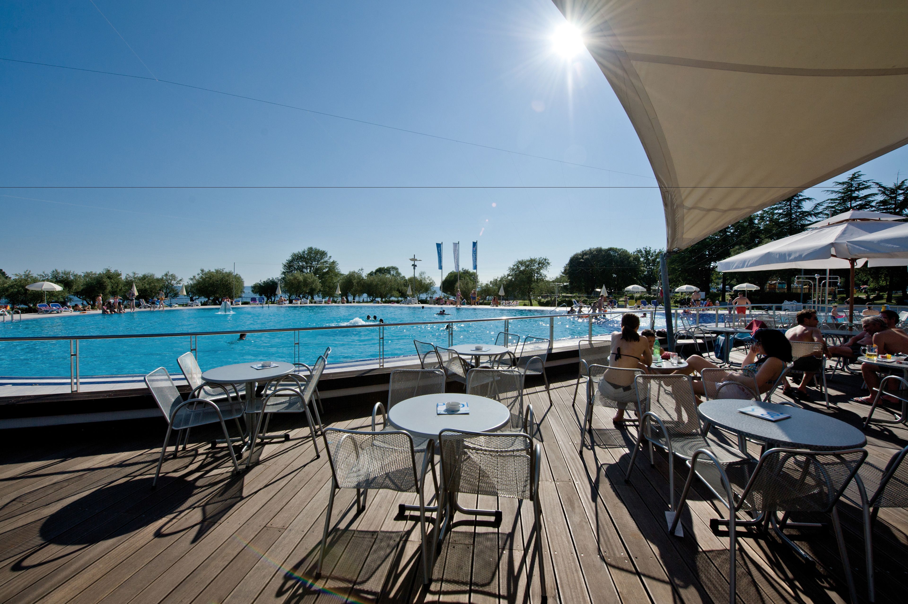A poolside area with tables and chairs, a pool, and a clear sky.