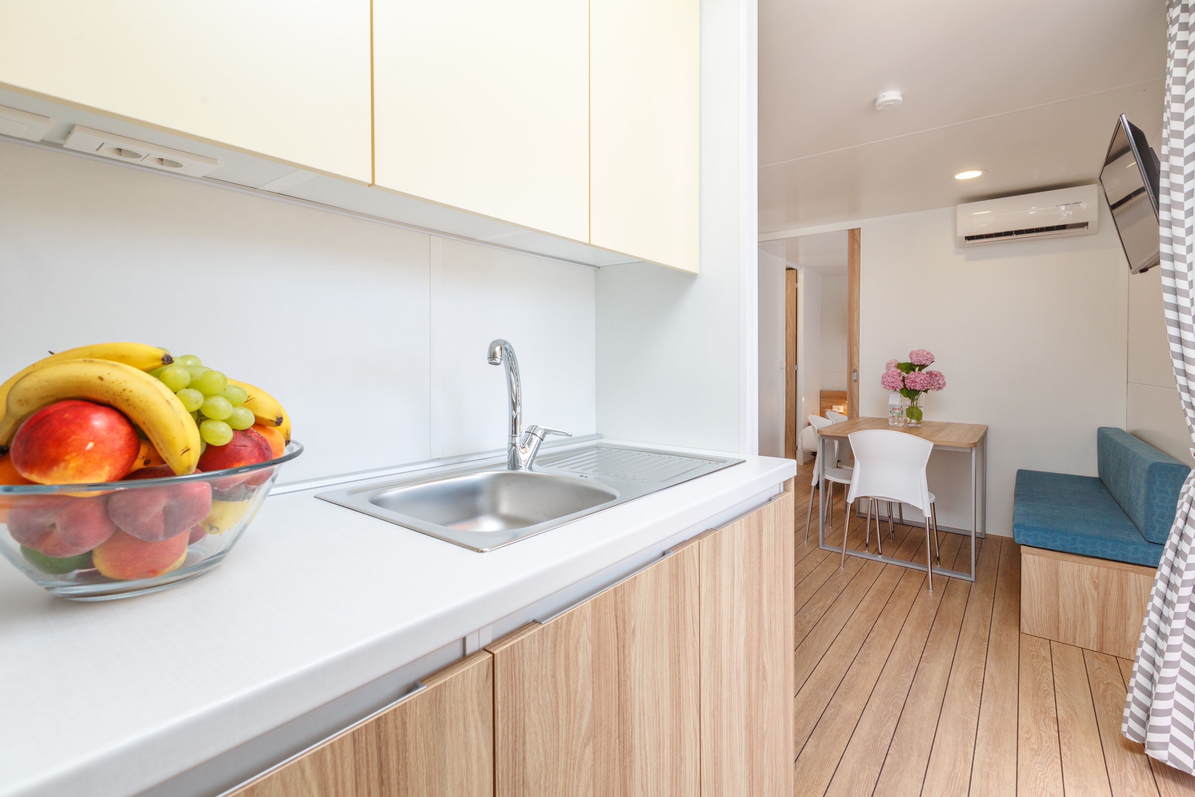 A modern kitchen with a fruit bowl, a sink, and a dining area with a blue sofa and a small table.