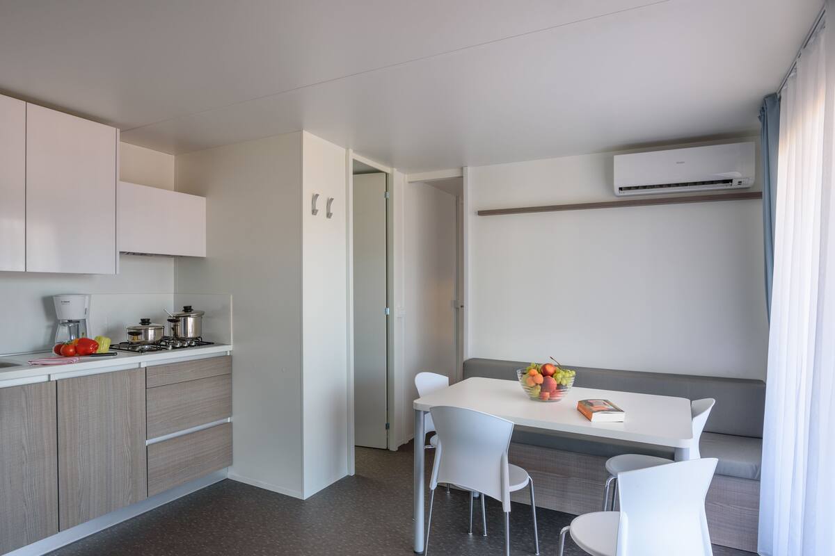 Une cuisine moderne avec des meubles blancs, une cuisinière à gaz et un coin repas comprenant une table et des chaises blanches.