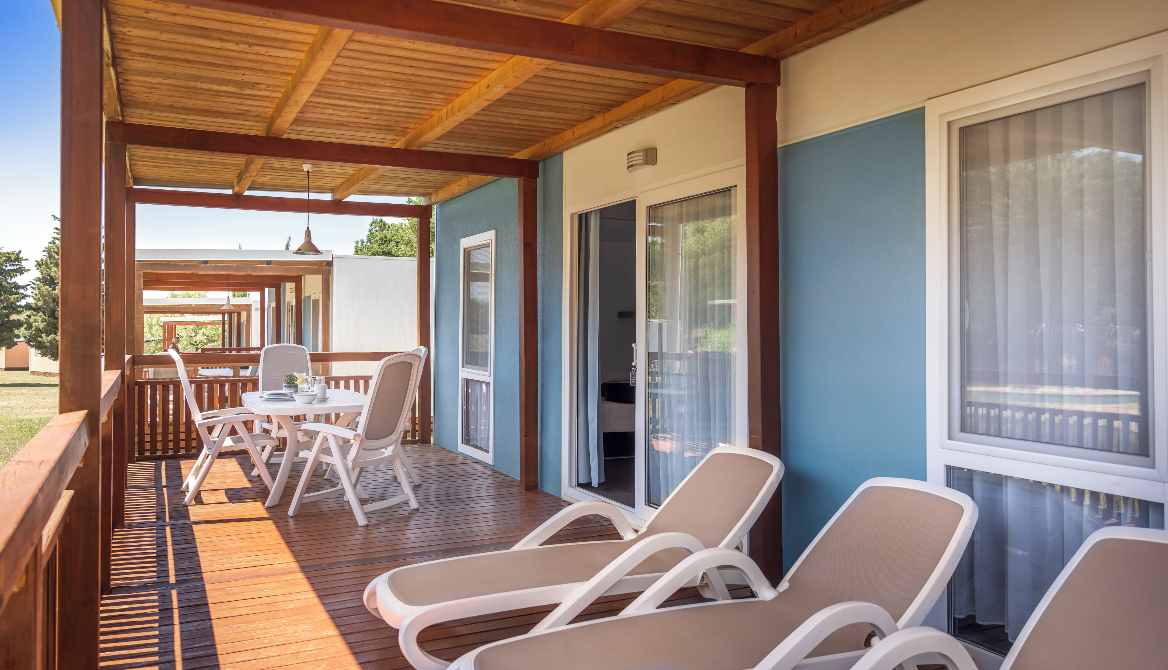 A covered outdoor seating area with wooden flooring, white chairs, and a table.