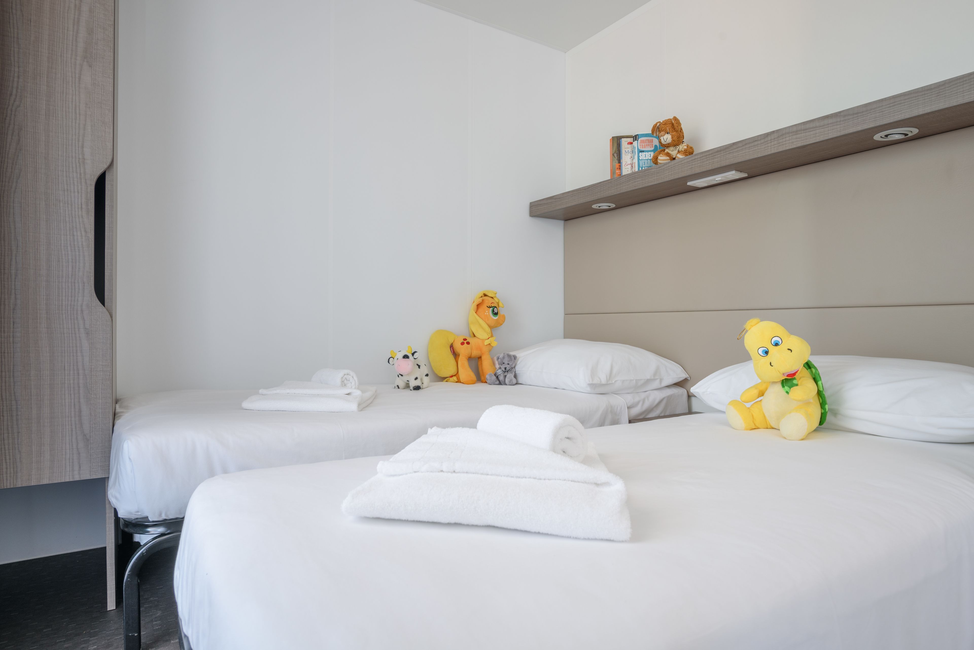Habitación de hotel con dos camas, ropa de cama blanca y peluches en las camas.
