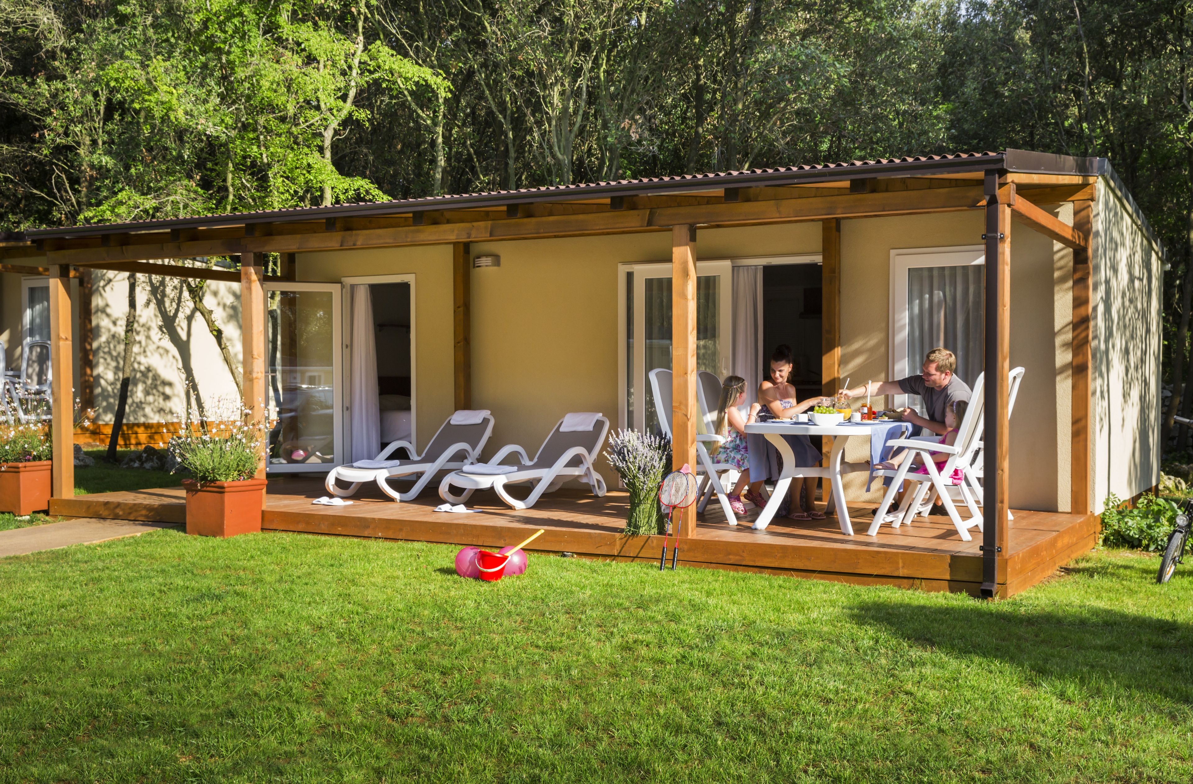 A covered outdoor dining area with a table and chairs, surrounded by a wooden deck and glass doors.